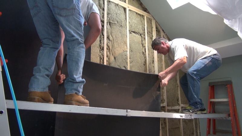 A crew from New England Soundproofing applies a sound-deadening, mass-loaded, sheet vinyl product called Sound Barrier HD to a party wall separating a condo stairwell from the unit next door. Materials like this vinyl and the special sound-absorbing rock-wool fiber insulation in the wall cavities can be used to absorb, deaden, and muffle sound vibrations from a variety of sources. Solutions are based on the nature of the sound source and the subjective perceptions of building occupants.