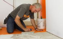 Tile contractor Tom Boucher of Integrity Tile, based in Kennebunk, Maine,  applies latex-modified Bostik Ditra-Set mortar to an Advantech subfloor to make a mortar bed for adhering Schluter Ditra decoupling underlayment membrane for a custom marble tile floor in a bathroom for a new house under construction next to the ocean south of Portland, Maine.
