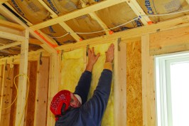 To insulate effectively, fiberglass batts need to fill the entire stud bay without being compressed. To insulate a wall, start by filling the full-width bays. Insert the batt from the top down, pushing it up against the wall plates. If the sides snag on rough lumber, run a putty knife along the side of the stud.