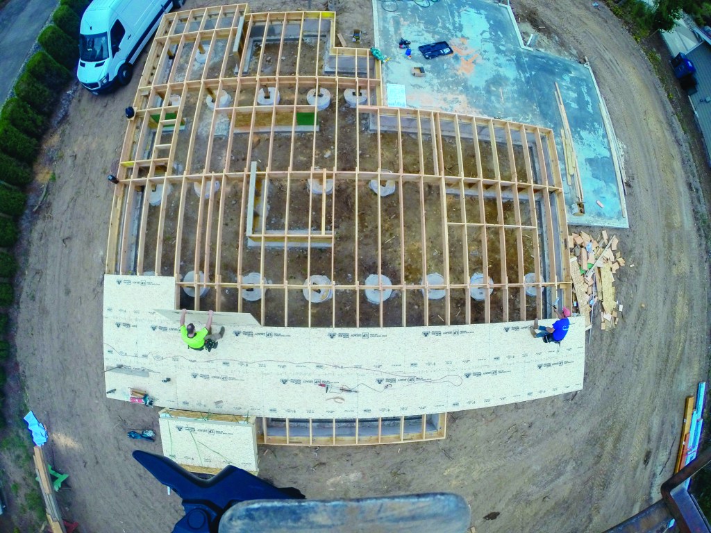Above is a bird’s eye view of the floor sheathing process. A crew of two works in harmony to sheathe this floor quickly and efficiently. The crew member on the right spreads glue on the joists while the crew member on the left takes sheets from the stack, drops them into place, and tacks them on layout. When the glue is spread for one course, the person gluing will take over dropping and tacking while his partner fastens the sheets with a screw gun.