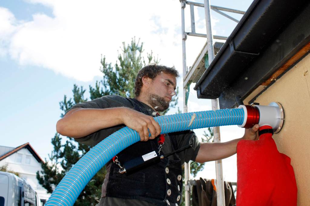 This photo from German equipment maker X-Floc shows the company's dry injection system for cellulose insulation in action. The back-pressure relief valve allows air to escape so that insulation can be uniformly delivered and compacted, while the red filter bag contains dust.