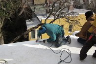 TPO single-ply membrane seams are heat-welded. Here, the installer warms up both the TPO membrane and TPO membrane flashing strip along an open roof edge using a special heat gun, which melts both pieces of a TPO roof joint. They are then pressed together with a hand roller to form a watertight seam.