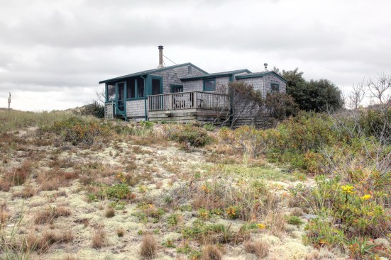 A view of the dune shack showing the main volume of the house stepping down to the bedroom and toilet room. Exterior deck is accessed from the screen porch.