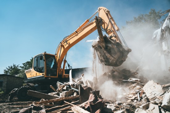 Destruction of old house by excavator. Bucket of excavator breaks concrete structure.