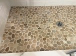 Irregular stone pebbles add a natural design element to a tiled shower but should be installed over a base with more pitch than normal to allow for better drainage. For ease of application, a good sanded high-performance grout rather than epoxy grout is recommended for use with natural stone pebbles.