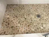 Irregular stone pebbles add a natural design element to a tiled shower but should be installed over a base with more pitch than normal to allow for better drainage. For ease of application, a good sanded high-performance grout rather than epoxy grout is recommended for use with natural stone pebbles.