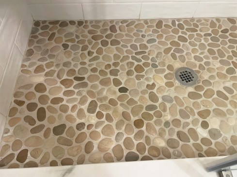 Irregular stone pebbles add a natural design element to a tiled shower but should be installed over a base with more pitch than normal to allow for better drainage. For ease of application, a good sanded high-performance grout rather than epoxy grout is recommended for use with natural stone pebbles.