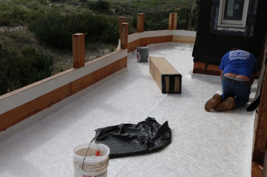 The next day the installer lays out the non-woven fiberglass mat on the deck, letting it extend up the walls about 6 inches. He also cut strips for the tops of the parapets.