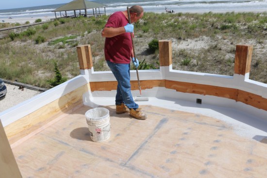 After rolling gelcoat on the parapets, the installer applies the finish to the transition areas.