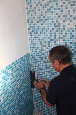 First slice through the mesh backing with a razor knife. Then slide a row (or rows) of tiles over with a flat taping knife until an acceptable grout
space is left along the corner.