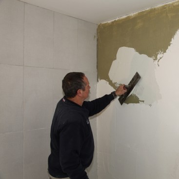 Wall prep for a glass-tile installation begins with a coating
of a liquid stress-crack membrane (the dark tan layer). Then add a coating of glass tile mortar over that.