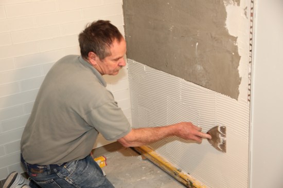 Spread an even layer of glass-tile mortar on the wall and comb it with a 1/4-inch square-notch trowel.