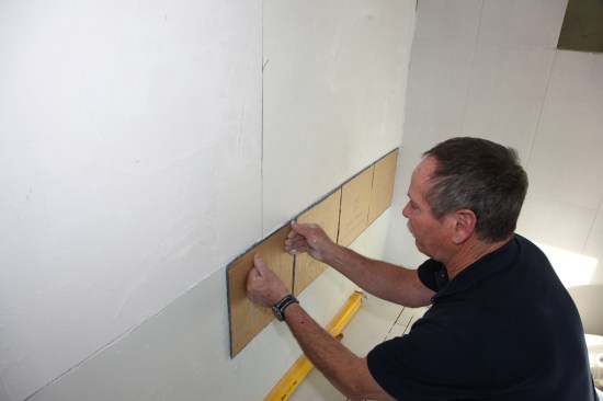 Starting at the horizontal layout line, press sheets of the mosaic tile into the mortar.