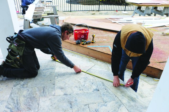 The original center point that the crew had used for laying out and framing the circular porch was covered by the new travertine tile on the porch floor. To re-establish that point, crew members mark a pair of chords, or straight lines, that connect two random points along the outside arc of the stone floor. Then they mark the center point of one chord.