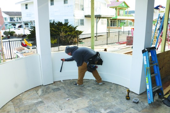 He taps the bottom rails down to the bottom of the panels using the rubber handle of a hammer before fastening them in place with stainless steel screws.