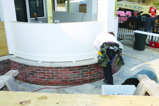 For the rails on the outside curve of the knee wall, the crew installs the same dimension top and bottom rails as on the inside. After cutting the bottom rail to length, a crew member screws it through the flat panel and into the knee-wall framing, working from one side to the other.