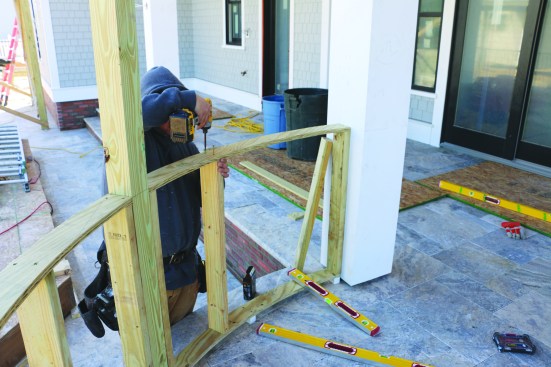After measuring between the layout points on the primary posts and cutting the plates to length, he installs intermediate 4x4 posts on stainless steel post bases that have been attached to the travertine with concrete anchors. He then frames the knee wall on top of PVC blocks that allow space for drainage below the framing.