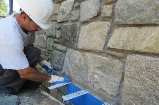 A mason puts the finishing touches on the reinstalled stone veneer; cleaning up the mortar around the corrugated weeps.