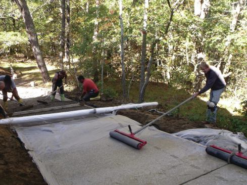 With the plastic covering the wet concrete, a crew member rolled a heavy steel roller over the surface, which compacted, consolidated, and smoothed the surface while preserving the voids in the concrete and ensuring that the plastic stayed in complete contact with the driveway surface so that hydration didn't happen too quickly. 