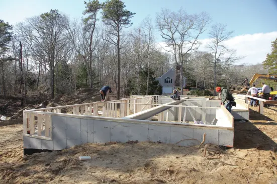 With such a long drop wall, it's important to make sure it is parallel with the foundation wall, which we confirm by measuring the distance between the rear and front walls at several places. We use 2x6s to brace the drop wall back to the steel, which we had tied to the front foundation wall earlier, providing us with a solid connection point.