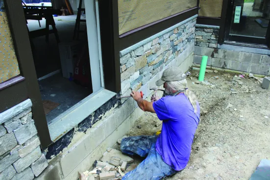 To create a solid toekick below each door, the crew cuts slabs of Pennsylvania bluestone to fit each spot. They remove any chunks of mortar left behind from installing the veneer.