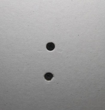 The top screw is driven properly, but the bottom screw is overdriven and has broken the paper around the screw head.