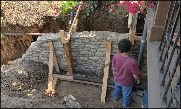 The 4-foot-plus-high standing section of wall was braced after plumbing up the wall. A pair of come-alongs attached to two steel anchor posts and 4-by wall braces were used to pulled the wall back to plumb; 2x4 angled bracing was reset after plumbing up the wall.