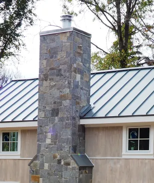 Roof intersection for a framed chimney clad with adhered stone.