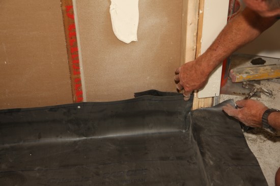 The membrane needs to be cut where it transitions from the vertical plane of the walls to the horizontal plane of the threshold. This area demands close attention to keep it waterproof. 
The first step is to cut the membrane tight to where the top of the threshold meets the jamb framing, allowing the membrane to wrap over the top of the threshold.