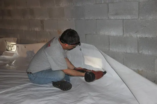 The installer fastens the poly to the block wall with pneumatic-driven nails and metal washers.