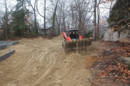 Using the skid-steer machine as both an earthmover and a smoother, George manipulates the grade in back of the house. He has to maintain a flat area for a patio immediately behind the house.