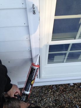 A bead of low-temperature caulk is squeezed in over the backer rod. Manny then smooths out the bead with his finger. Note that the joint between the siding and the window trim has also been caulked.