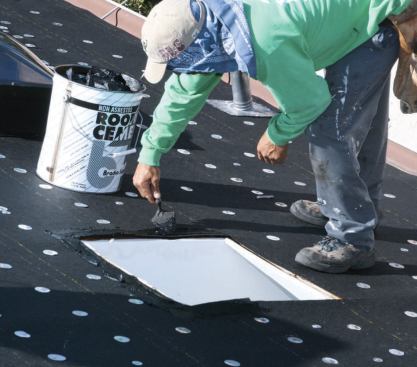 A reroof job usually includes new self-flashing skylights with integral curbs. A roofer applies cold asphalt cement to the new asphalt felt paper.