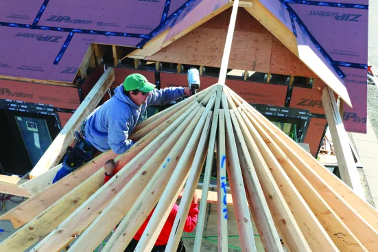 A crew member nails the tops of the rafters at the peak ...