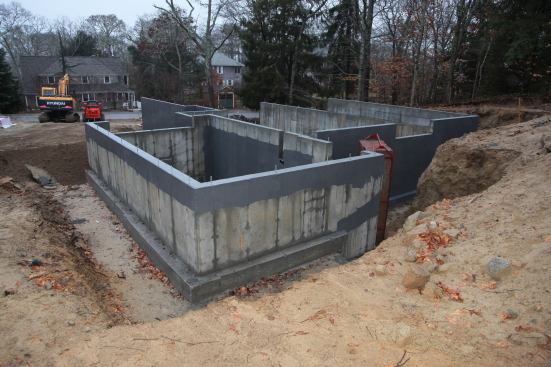 The stepped foundation is poured on footings and then given a waterproof coating. The garage foundation in the foreground will be filled up to the slab level. An integral shelf seen in the far wall of the foundation will support the floor framing and allow the floor framing to be below grade.