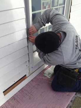 After aligning the edge of the flashing tape with the guideline, Manny carefully presses the tape into the corner of the nailing flange. The free edge of the tape then tucks behind the siding that had been lifted away from the wall slightly when the opening was being prepped.