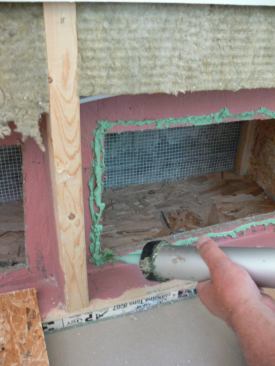 Once the wall cavities were dried, the crew applied patches over the OSB air barrier using pieces of ZIP sheathing. Here, a worker applies adhesive caulk sealant to the original OSB air barrier before fastening on the patch.