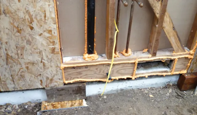When wall sheathing is set in beads of polyurethane foam, temporary blocks at the base make it easier to position the sheet without smearing the sealant.