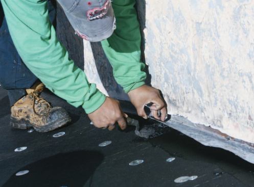 The roofer applies cold asphalt cement under the flashing.