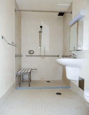 The barrier-free shower is equipped with a flexible rubber dam that helps contain water without inhibiting wheelchair access; note the second floor drain under the sink.