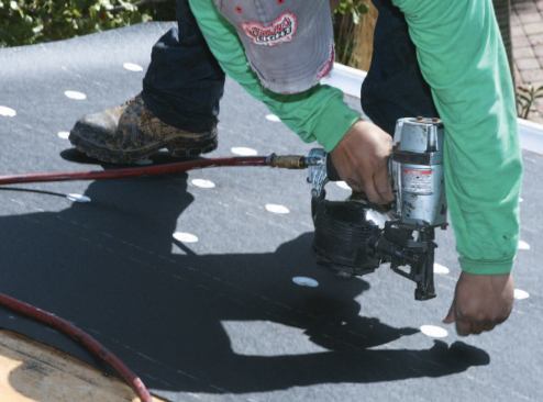 Fresh courses of 30-pound asphalt felt, attached with ring-shank nails driven through metal disks, replace the 15-pound felt the crew has just torn off.
