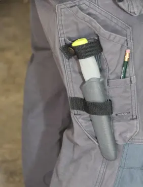 The sheath fits through a loop on the pants—which keeps it from swinging or flopping around. The knife “clicks” into the sheath and should not fall out. As an added measure, these pants include a piece of webbing that snaps around the end of the hilt. This particular knife and sheath are made by Mora.