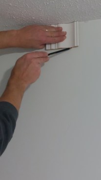 Using a piece of scrap cut to match the distance that the crown will extend downward from the ceiling, the author can mark lines where the bottom of the crown will sit. Doing so helps to ensure that the molding is installed evenly around the room.
