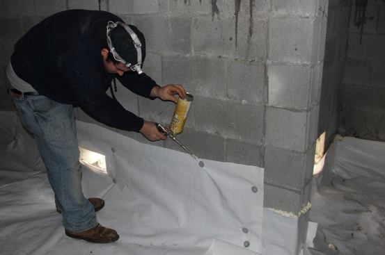 Air-driven masonry nails and metal disks hold the poly ground cover to the concrete block walls at the perimeter. The crew seals the joint between the poly and the masonry using adhesive foam sealant.