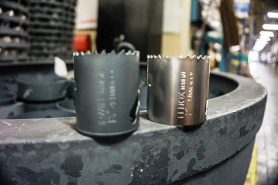The next step is heat treating—which takes place in large vat-like furnaces where temperatures exceed 2,000 degrees. It takes many many hours to heat treat the pieces. The hole saws go in bright (like the piece on the right) and come out a dull grey color (like the one on the left).