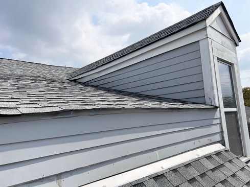 No cut back or step flashing. Siding running down to the roof shingles is wicking water and is at risk of failing. Worse, this roof also lacks step flashing. The combined errors are causing water leaks inside the dormer.