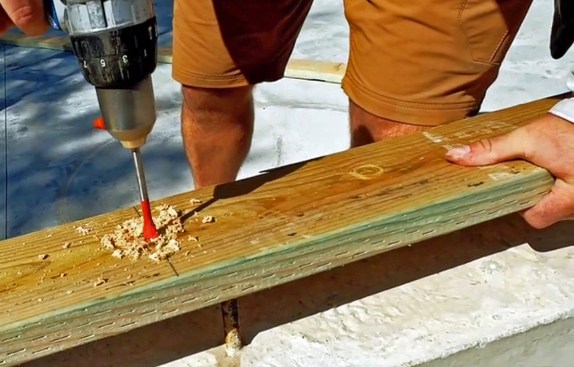 He then pulls the board back to his chalk line, measures the distance, and drills the holes.