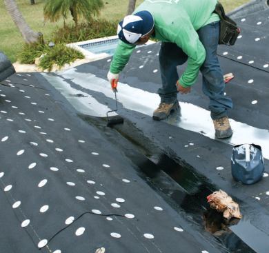 Before hot mopping begins, a roofer coats metal valley flashings with asphalt primer.