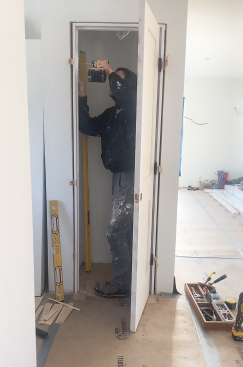 After hanging the door, he aligns the latch side, keeping an even reveal (the gap between the door and the jamb). He first secures the top of the jamb. He checks to be sure the door hits the stop evenly, then secures the bottom, and finally shims behind the strike plate until the gap is correct.