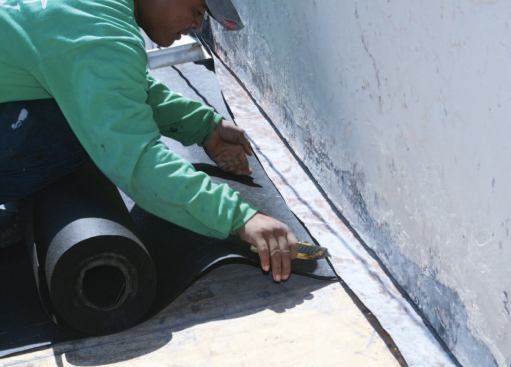 A roofer slips the new felt under the existing sidewall flashing, which has been scraped clean.